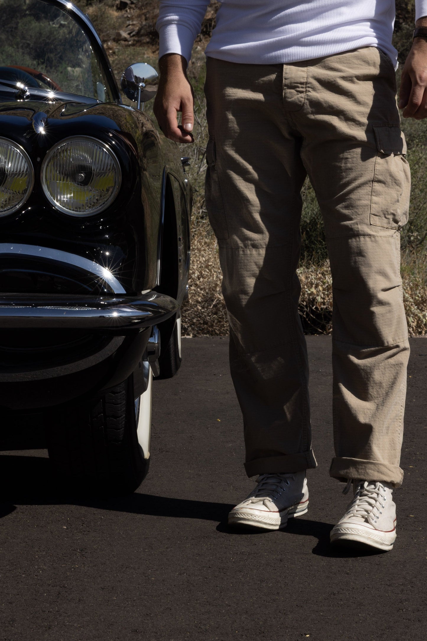 Person standing next to a vintage car on a road with desert landscape in the background